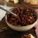 A bowl of bacon jam with a crostini on a cutting board.
