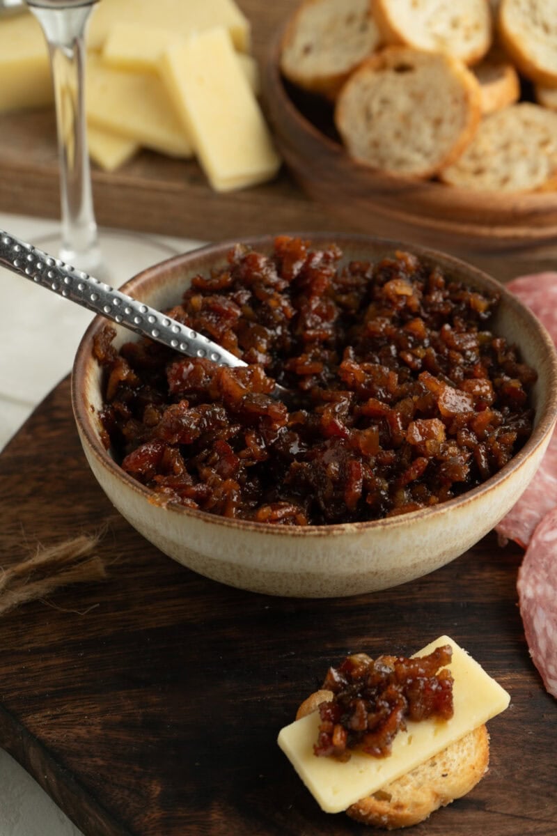 A bowl of bacon jam with a crostini on a cutting board.