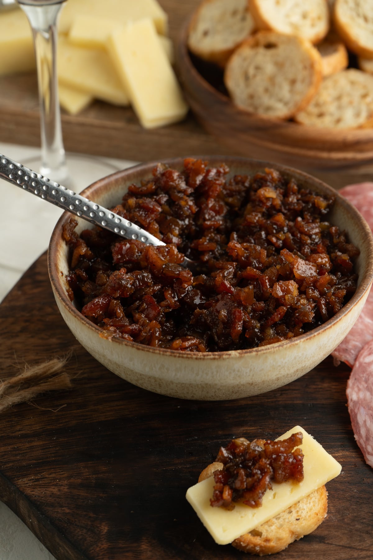 A bowl of bacon jam with a crostini on a cutting board.